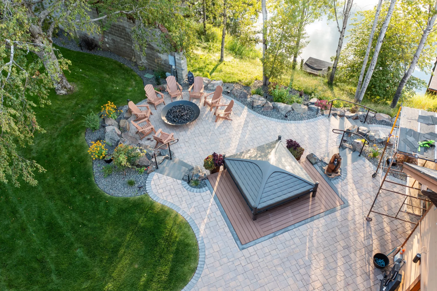 Representative Legacy Landscapes portfolio: aerial view of a landscaped backyard with a circular fire-pit seating area, curved paving, lawn, trees, and a covered outdoor structure.