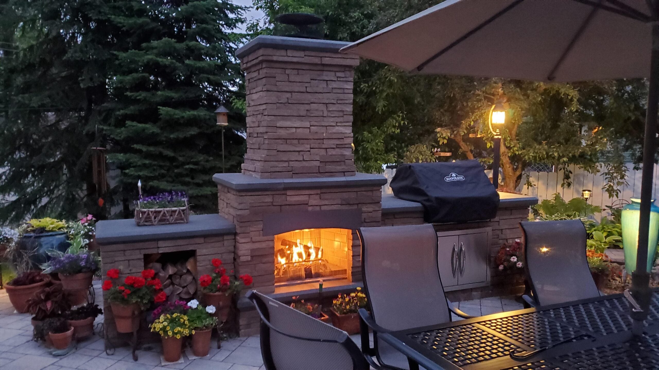 Representative Legacy Landscapes portfolio: masonry outdoor kitchen with a built-in grill, patio seating, planters, and evening lighting.