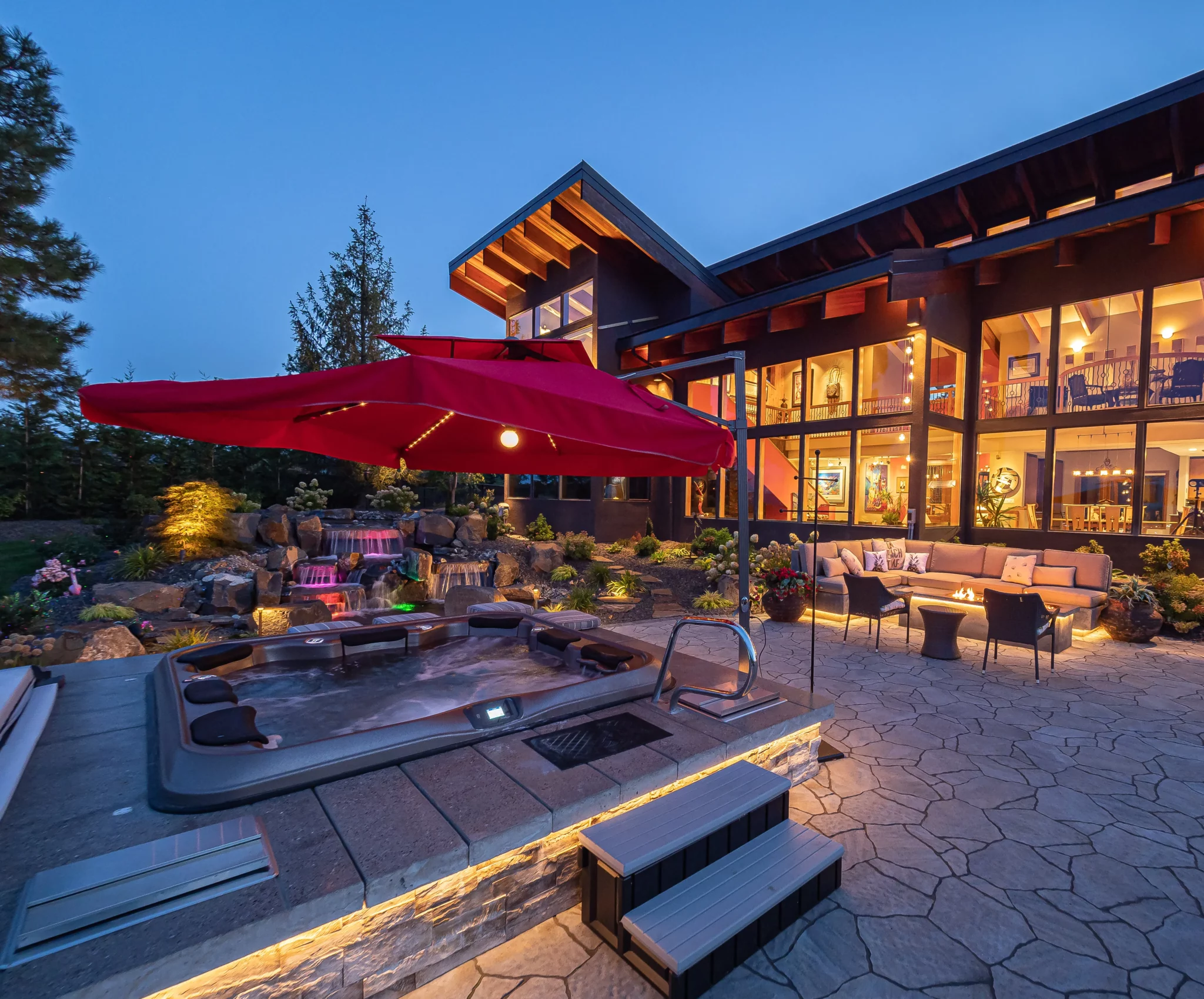 Representative Legacy Landscapes portfolio: outdoor entertaining space with poolside seating, stone paving, umbrellas, and a modern residential setting.